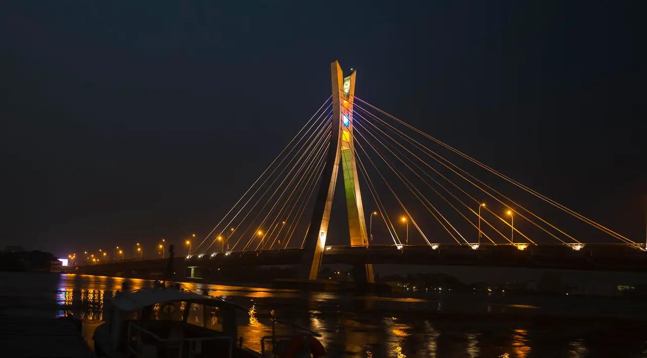The Lekki-Ikoyi Link Bridge lit at night, with street lights along the deck reflected in the lagoon.